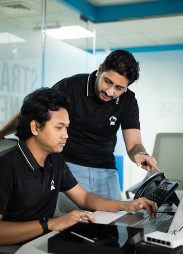 Two IT technicians collaborating on computer software configuration and system troubleshooting at a desk