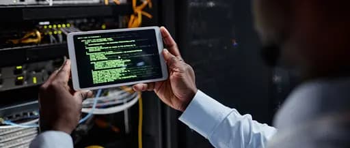 Network specialist using a laptop computer to monitor systems while standing inside a server room
