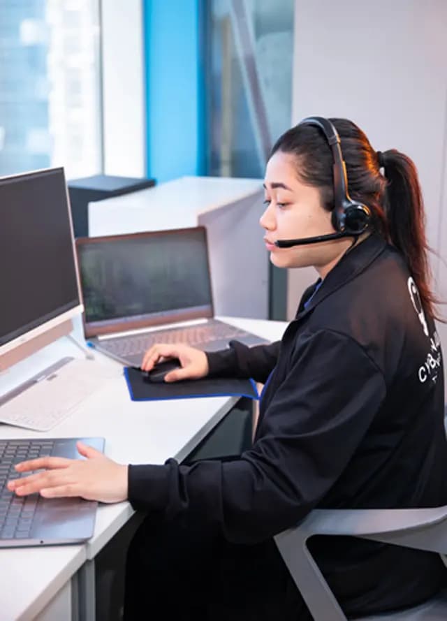 An IT maintenance support professional works at a desk equipped with multiple computer monitors and laptops