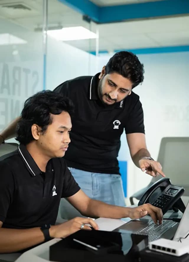 Two IT technicians collaborating on computer software configuration and system troubleshooting at a desk