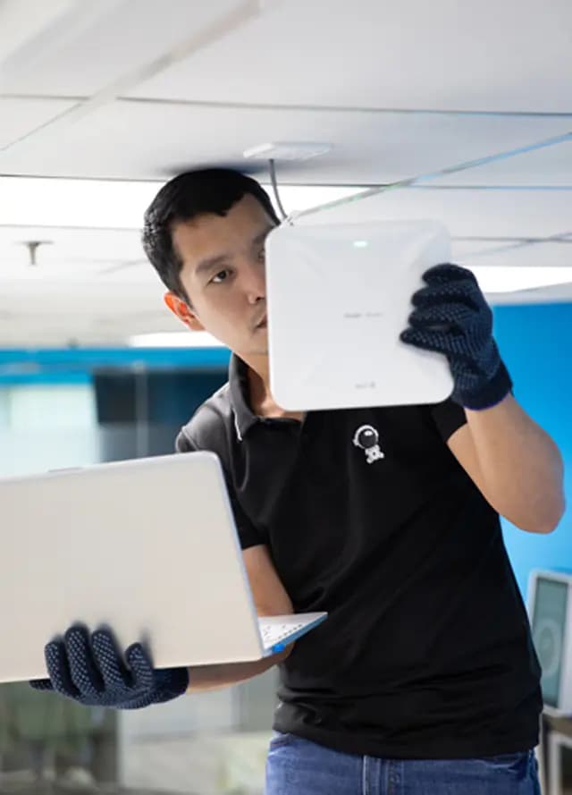 IT technician configuring a white wireless access point while holding a laptop